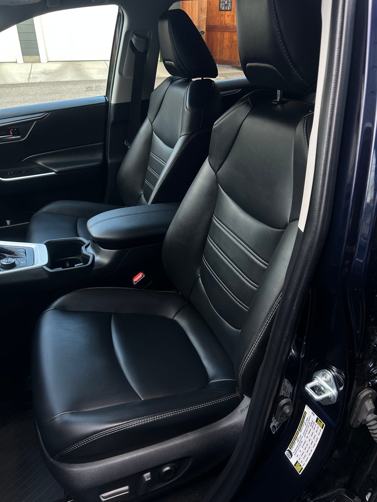 Black leather car interior with front seats, steering wheel, and center console visible through open drivers side door