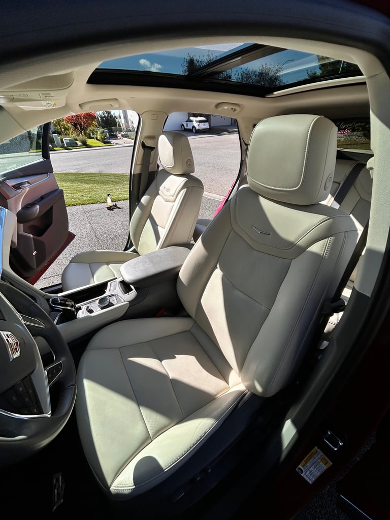 Interior view of a car with tan and gray leather seats, panoramic sunroof open, showing dashboard and residential driveway